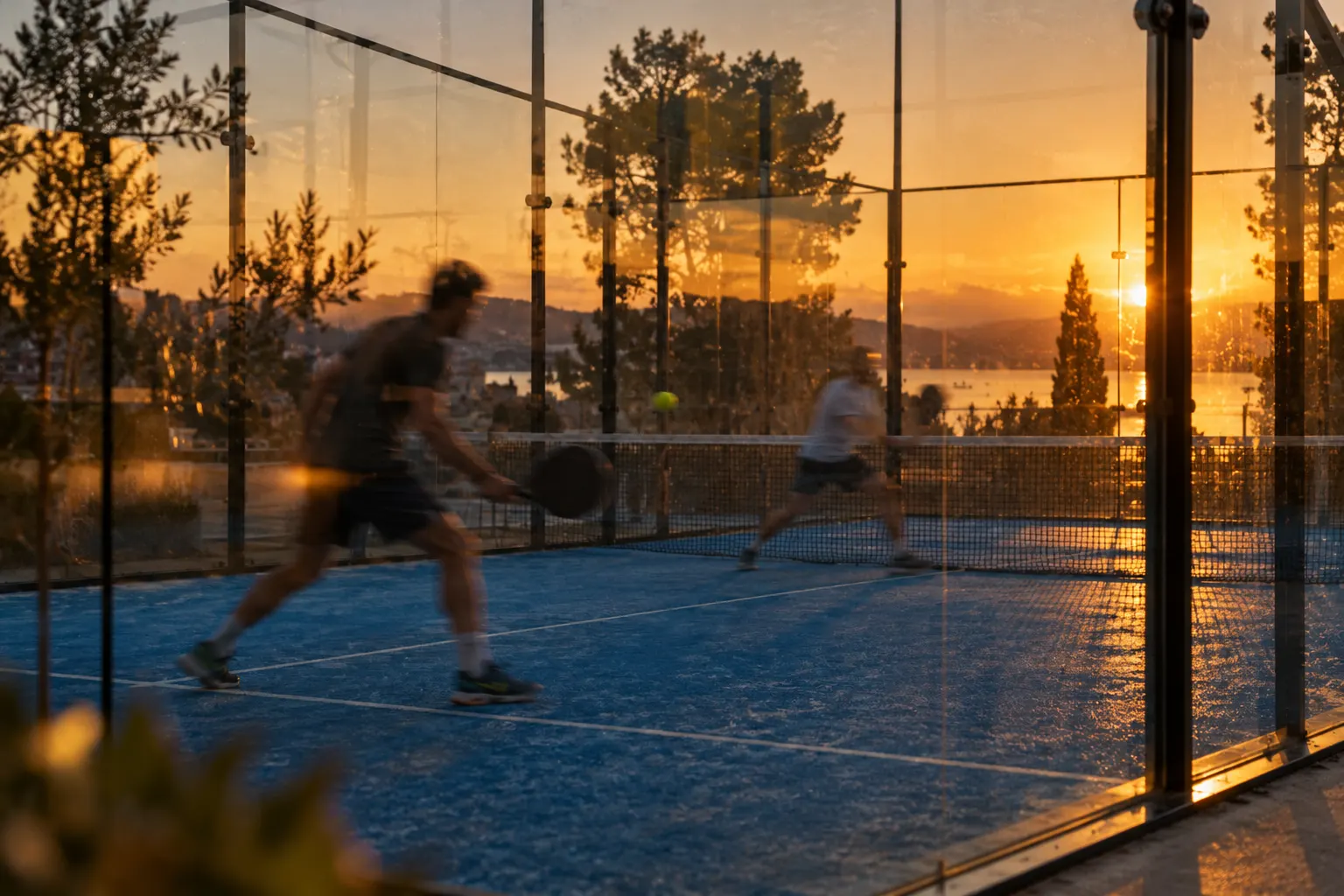 Deux joueurs de padel en plein échange, vus à travers la vitre du terrain au coucher du soleil